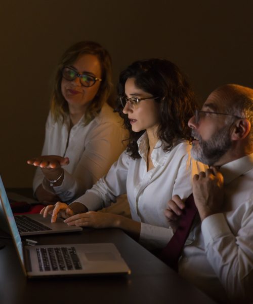 Colleagues discussing work in dark office. Side view of professional businessman and businesswomen working with computers in dark office. Business and technology concept